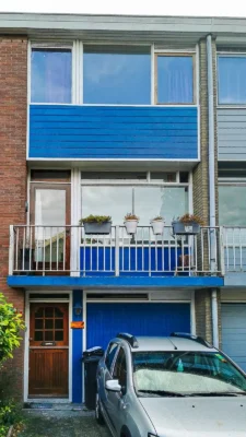Voor de renovatie: gevel van een rijwoning in Zoetermeer met oude houten kozijnen, blauwe gevelbekleding op het balkon en houten voordeur vóór de modernisering van de kozijnen en gevel door Avalanche Windows.