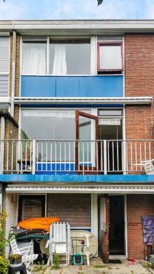 Achtergevel van de woning in Zoetermeer vóór de renovatie, met oude houten kozijnen, blauwe gevelpanelen en balkondeuren vóór de vervanging van de kozijnen en gevelmodernisering door Avalanche Windows.